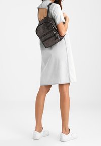 Sac à dos noir en sequins avec une forme arrondie, doté d'une poignée supérieure et de bretelles ajustables, porté avec une robe en jean clair à manches courtes.