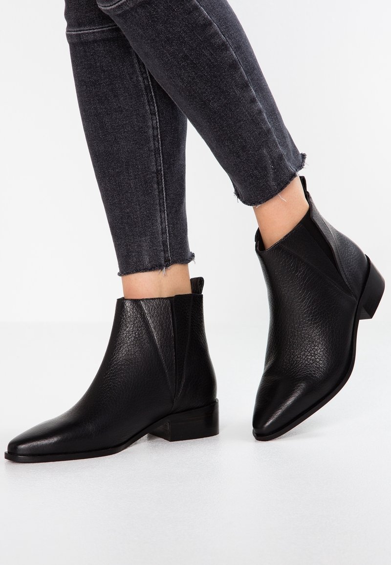 Bottes à la cheville en cuir texturé noir avec bouts pointus et talons bas, portées avec un jean skinny gris foncé à ourlet effiloché.