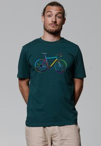 T-shirt vert à manches courtes présentant un contour multicolore d'une bicyclette. Tissu lisse avec un col rond et une coupe décontractée.