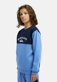 Sweat-shirt color block bleu et marine à col rond, avec un logo graphique. Texture douce et poignets côtelés, assorti à un pantalon assorti.