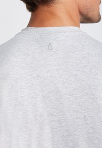 Grijze kraagloze t-shirt met korte mouwen, gemaakt van een zachte katoenmix. Bevat een klein geborduurd logo aan de achterkant van de hals. Zachte textuur.