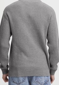 Harmaa neulepaita, jossa on texturoitu kuvio, pitkät hihat ja ribbaushelma. Takakuvassa näkyy rento istuvuus ja hienovaraista yksityiskohtaisuutta.