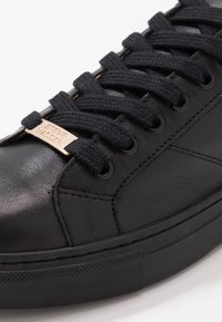Czarne skórzane sneakersy z grubymi czarnymi sznurówkami i małym złotym tagiem z wygrawerowanym napisem "Steve Madden" w przedniej części sznurowania.