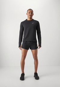 Camisola desportiva preta de manga comprida com aberturas para os polegares, combinada com calções pretos e sapatilhas pretas. Logo da Nike na camisola e nos calções.