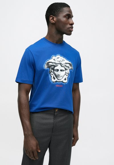 Modré bavlnené tričko s výraznou grafikou Medusy v sivej farbe s detailnou výšivkou. Kombinované so šedými nohavicami na mieru.