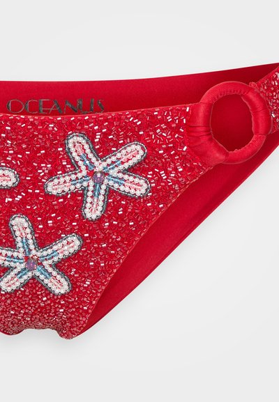 Röd bikiniunderdel med pärlformade sjöstjärnemönster i vitt, blått och rosa. Har en texturerad yta och en cirkulär hårdvaruaccentsdetalj på sidan.