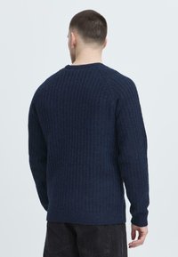 Navy knit sweater with textured pattern, round neckline, and ribbed cuffs. Long sleeves, straight fit, and medium weight fabric.