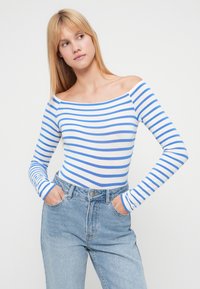 Τοπ με ανοιχτούς ώμους και μακριά μανίκια, με μπλε και λευκές ρίγες, κατασκευασμένο από απαλό ύφασμα, συνδυασμένο με ανοιχτό μπλε τζιν ψηλόμεσο.