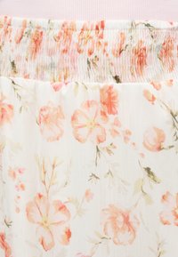 Ceinture élastique avec couture smockée sur tissu blanc présentant un motif floral pêche et rose clair avec des tiges et des feuilles verdâtres.