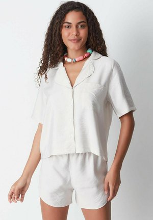 White short-sleeve pajama set with a collared button-up top and matching shorts. Fabric appears soft with a subtle sheen. Includes a chest pocket.