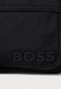 Fekete szövet pénztárca, amely egy sima felületű, struktúrált logót kínál, egyszerű kialakítással, fedéllel záródik, és varrott széllel rendelkezik.