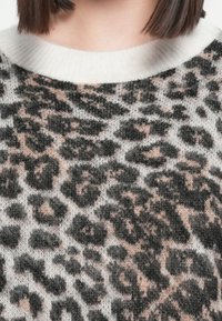Pleteni pulover s uzorkom leoparda u crnoj, sivoj i mekoj ružičastoj boji, s bijelim rebrastim okovratnikom i različitim teksturama.