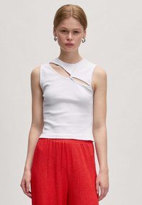 Witte mouwloze top met uitsnijdetails bij de hals, gemaakt van geribbeld stof; gecombineerd met felrode, textuur brede broek.