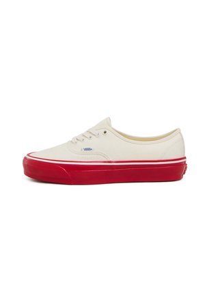 Cremefarbene Leinenschuhe mit roter Gummisohle, weißer Naht und strukturiertem Zehenkappen, ausgestattet mit Schnürsenkeln und einem blauen Logoschild an der Seite.