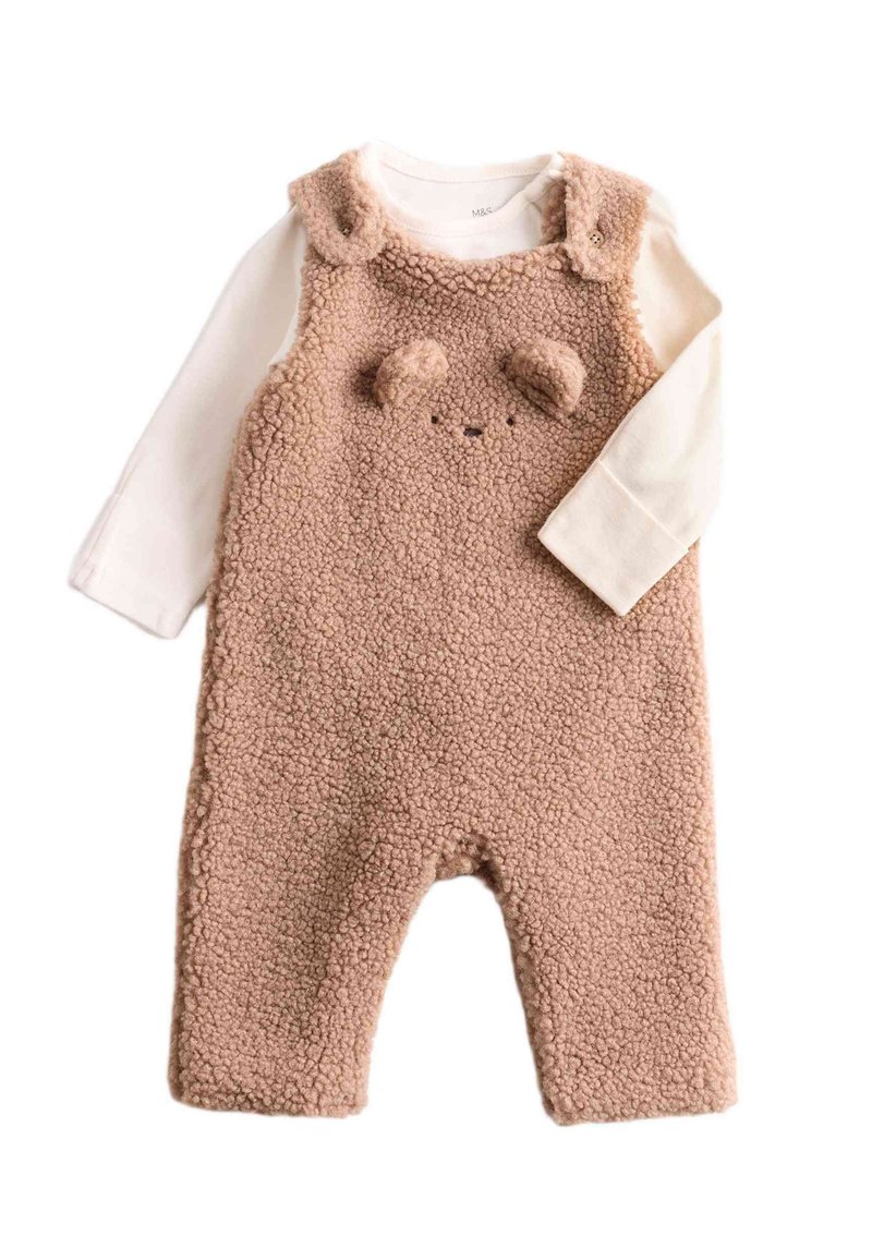 Både overall i beige med en strukturerad yta, med ett björnhuvuddesign, runda öron och en fastsydd långärmad vit skjorta under.