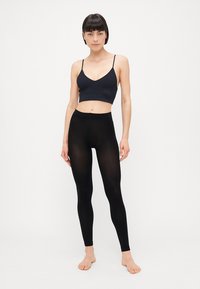 Svart sømløs bralette med tynne stropper, paired med svarte leggings. Begge plaggene har et glatt, elastisk stoff og et tettsittende design.
