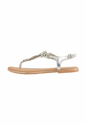 Sølv metalisk flad sandal med en dekorativ rhinestone-strop, tan sål og justerbar ankelspænde for sikker pasform.