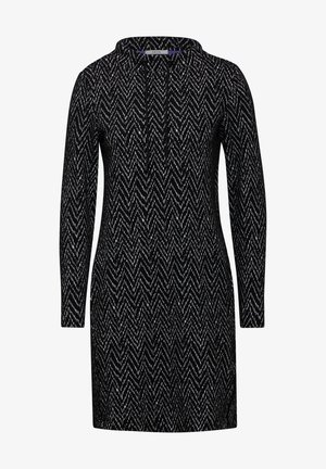 Zwarte jurk met lange mouwen, voorzien van een chevronpatroon in het wit. Het ontwerp heeft een kraag en een rechte snit. Gemaakt van gestructureerde stof.