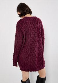 Übergröße burgunderroter Strickpullover mit strukturiertem Kabelmuster, geripptem Saum und langen Ärmeln. Leicht strukturiertes und gemütliches Material.