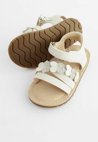 Weiße Sandalen mit zwei breiten Lederriemen, einem gepolsterten Fußbett und floralen Verzierungen mit silbernen Akzenten im oberen Bereich.