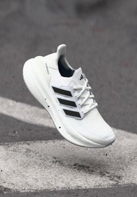 Białe buty sportowe z teksturowanym wkładem z dzianiny, z czarnymi trzema paskami, sznurowadłami oraz wyściełaną podeszwą z wyraźnym logo.