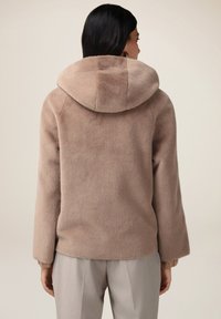 Faux fur jakke i lys beige med en stor hætte, der har en blød struktur, brede ærmer og ribbede manchetter.