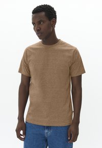 Brown, short-sleeve t-shirt with a textured surface, round neckline, and a loose fit, paired with blue denim jeans.