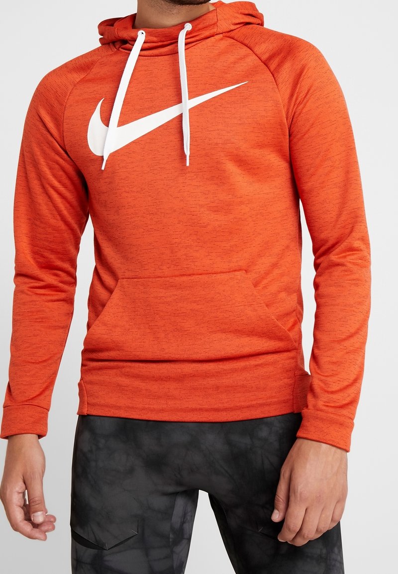 Sweat à capuche orange en tissu texturé, avec un grand logo Nike blanc sur la poitrine et des cordons blancs. Comprend une poche avant.