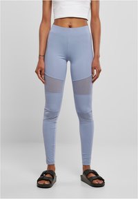 Leggings taille haute bleu clair avec des accents en mesh au milieu des cuisses ; fabriqués en tissu lisse et extensible. Assortis à des sandales noires.