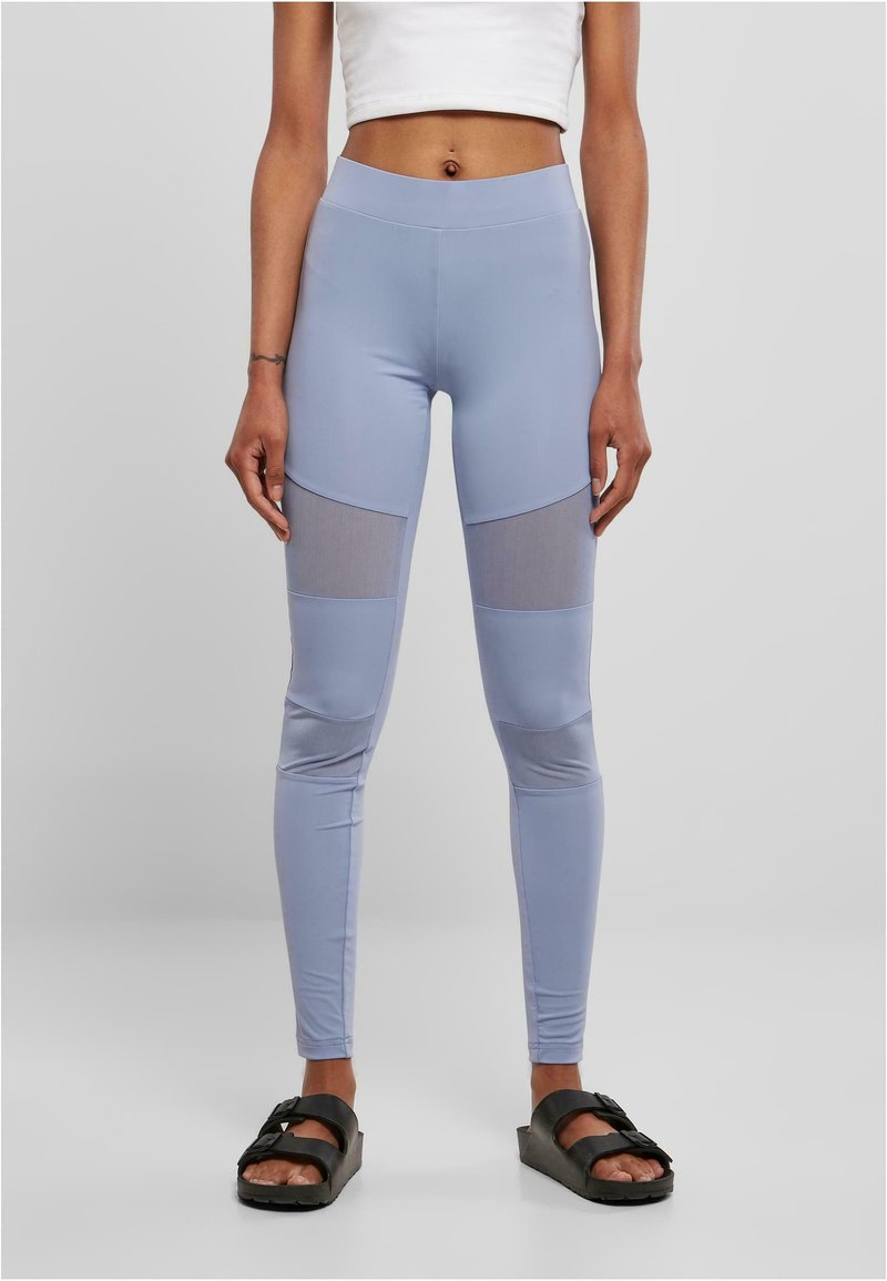 Leggings taille haute bleu clair avec des accents en mesh au milieu des cuisses ; fabriqués en tissu lisse et extensible. Assortis à des sandales noires.