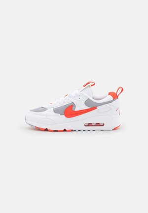 Baskets blanches et grises avec un swoosh Nike orange vif et des accents, semelle à air visible et languettes sur la languette et le talon.