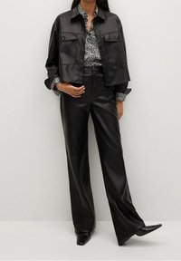 Veste en cuir noire courte avec deux poches devant, associée à un blouse à motifs noir et blanc et à un pantalon large en cuir noir.