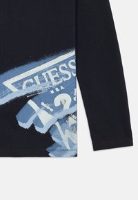 Black long-sleeve shirt with blue and white distressed Guess logo and question mark graphic on the lower side near the hem.