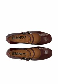 Zapatos de charol burdeos con punta cuadrada, que cuentan con dos correas aseguradas por hebillas de plata y una plantilla acolchada de color marrón claro.