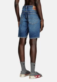 Shorts in denim blu scuro, di lunghezza media con orlo sfrangiato, due tasche posteriori e un'etichetta in pelle in vita. Abbinati a calzini grigi e scarpe.