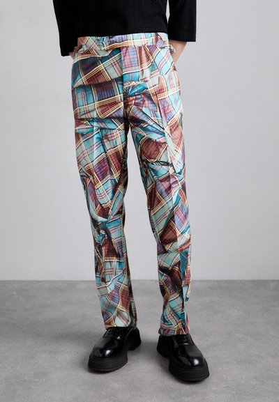 Pantalons à carreaux colorés présentant des motifs bleus, rouges et jaunes, avec une texture lisse et une coupe droite. Associés à des chaussures noires.