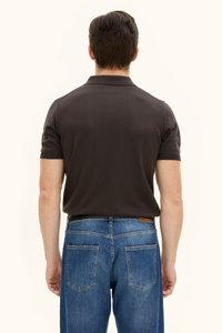 Brun pikétröja med korta ärmar och krage, kombinerad med blå jeans i denim med två bakfickor och en läderlapp på midjebandet.