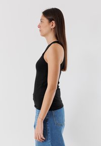 Top a canotta nera dal design aderente, abbinato a jeans a vita alta di color blu chiaro. Il tessuto sembra liscio senza pattern visibili.