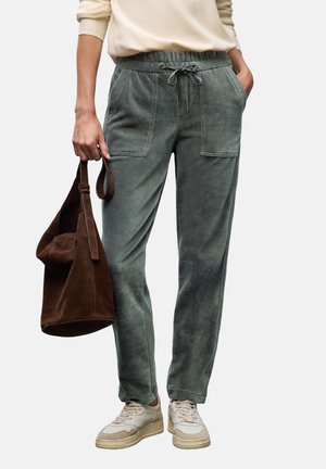 Person wearing gray-green corduroy jogger pants with large front pockets, beige sneakers, cream sweater, and holding a brown suede handbag.