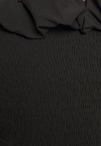 Abito nero con un design smocket testurizzato e un corpetto arricciato. Il tessuto appare morbido e leggermente elastico.