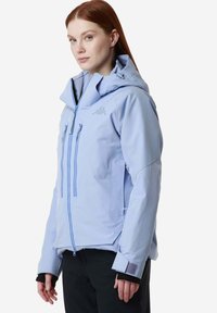 Giacca impermeabile azzurro chiaro con cappuccio, chiusura frontale con zip e due tasche sul petto. Presenta polsini elasticizzati e un design testurizzato.