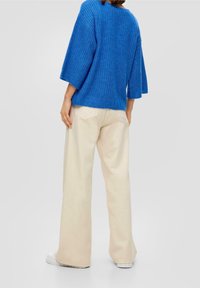 Maglione blu a maglia con vestibilità ampia e maniche a lunghezza gomito, abbinato a pantaloni a gamba larga beige chiaro e scarpe bianche slip-on.