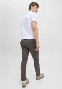 Sive hlače od pamuka sa slim fit krojem. Uparene s bijelim polo majicom i bež cipelama, imaju zavrnute manžete i diskretne stražnje džepove.