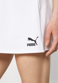 Gonna sportiva bianca realizzata in tessuto liscio con il logo PUMA nero vicino all'orlo. La gonna presenta un design semplice e pulito con una linea dritta.