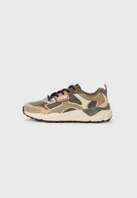 Zapatillas de camuflaje que presentan una combinación de materiales en marrón, beige y verde, una entresuela blanca gruesa y cordones negros con acentos amarillos.