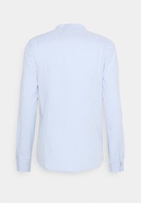Ljusblå långärmad skjorta med mandarin-krage. Strukturera tyg, knäppning vid ärmsluten och en rundad fåll. Inga synliga logotyper eller mönster.