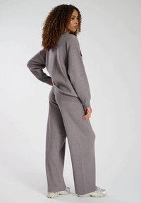 Grå, oversized sweatshirt och vida byxor i mjukt, texturerat material. Outfiten har en avslappnad passform och ribbstickade muddar.