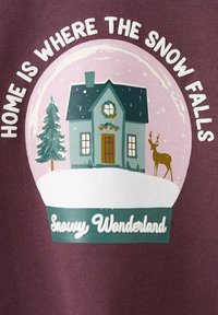 Grafika zobrazuje zelený dům s věncem, obklopený sněhem a stromem, umístěný v sněhové kouli. Text říká: "Domov je tam, kde padá sníh."