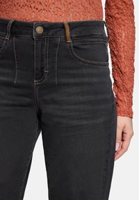 Jean en denim noir avec une coupe slim, présentant une taille texturée, des coutures contrastées et un style classique à cinq poches.