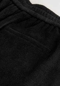 Zwarte ribstof broek met een gestructureerd oppervlak en een elastische tailleband. Inclusief een klein, discreet zijzakje.